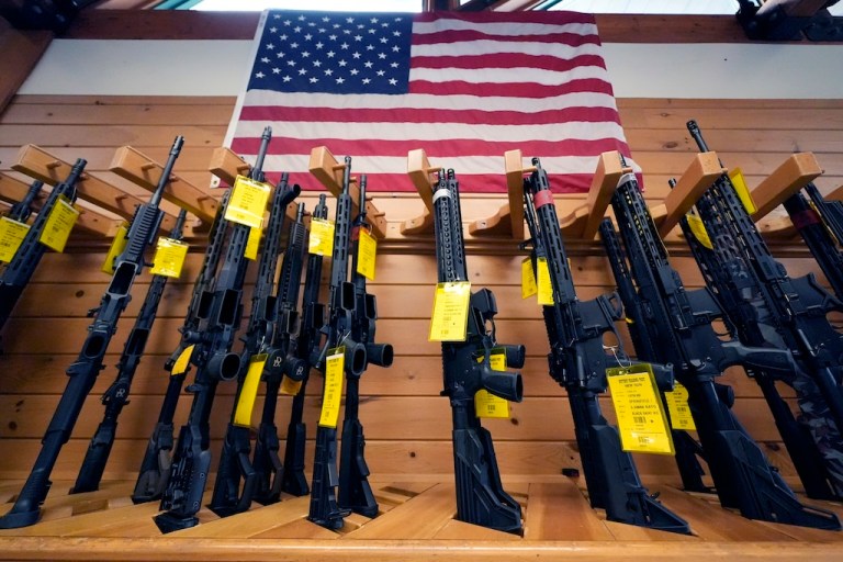 A variety of AR-15-style rifles are displayed under an American flag at the Kittery Trading Post.