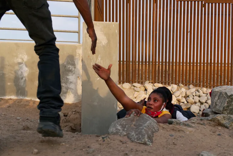 A Haitian migrant family member reaches out for help while emerging from a rocky canal adjacent to a gap in the U.S. border wall.