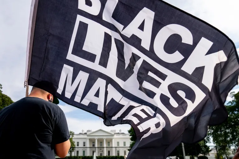 FILE - A man carries a Black Lives Matter flag in Lafayette Square outside the White House on the fourth night of the Republican National Convention, Aug. 27, 2020, in Washington. (AP Photo/Andrew Harnik, File)
