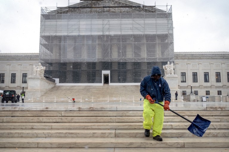 A worker shovels snow and ice in front of the Supreme Court.