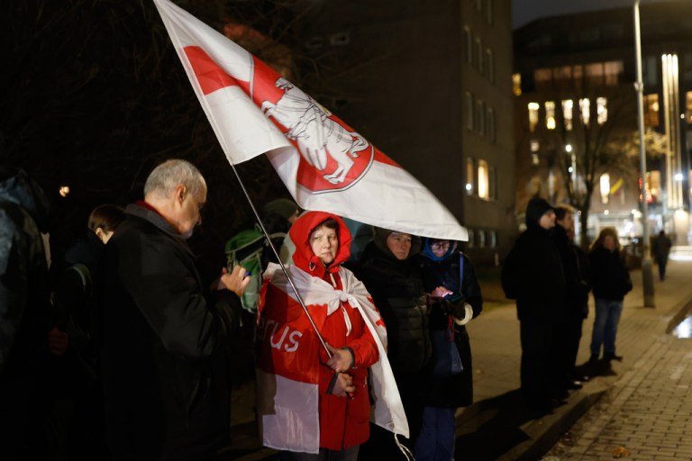 A woman holds an Old Belarusian flag as she stands waiting released Belarusian prisoners at the U.S. Embassy in Vilnius, Lithuania, on Saturday, Dec. 13, 2025. (AP Photo/Mindaugas Kulbis)