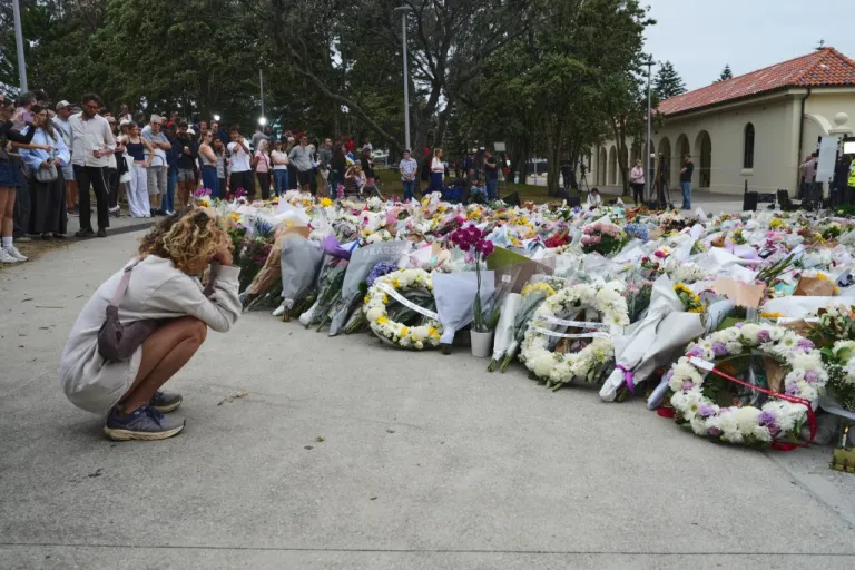 A young woman kneels down by a floral tribute by the Bondi Pavilion.