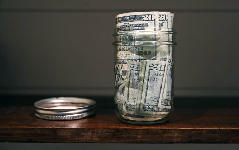A canning jar filled with money sits on a shelf.