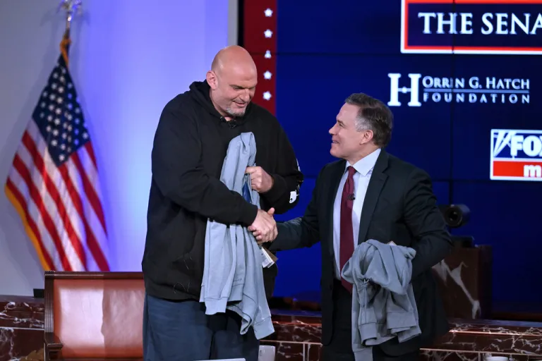 Sen. John Fetterman (D-PA) and Sen. Dave McCormick (R-PA) shake hands after being presented with hoodies from the Edward M. Kennedy Institute for the Senate after participating in a debate.