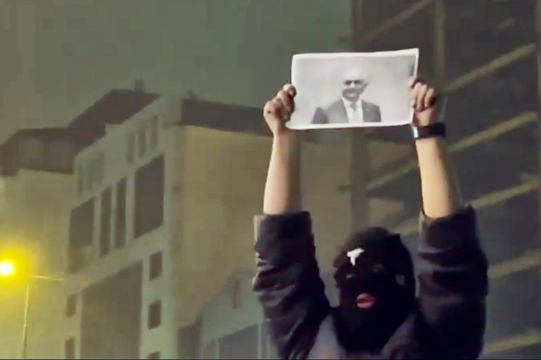 In this frame grab from video obtained by the AP outside Iran, a masked demonstrator holds a picture of Iran's Crown Prince Reza Pahlavi during a protest in Tehran.