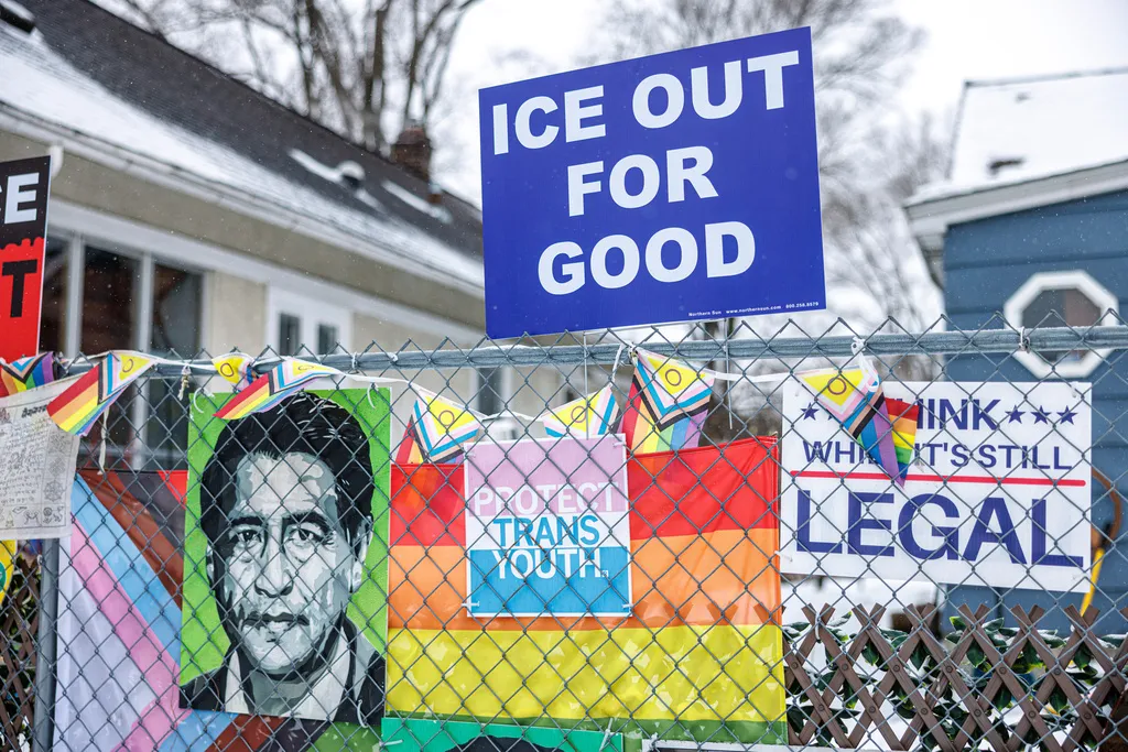 A sign reading "ICE Out for Good" is displayed above a chain-link fence decorated with pride flags and advocacy posters in a residential neighborhood on Wednesday, Jan. 21, 2026, in Minneapolis.