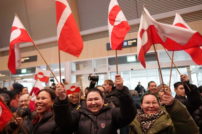 People wave by national flags while listening a speech of Greenland Minister for Foreign Affairs and Research Vivian Motzfeldt after her arrival at airport of Nuuk, Greenland, on Tuesday, Jan. 20, 2026. (AP Photo/Evgeniy Maloletka)