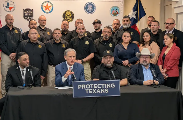 four people sitting behind a desk and several people standing behind them