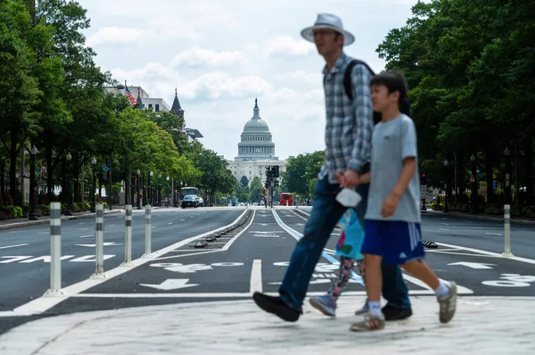 A man and boy cross Pennsylvania Avenue with the Capitol in the background, in Washington, Thursday, Aug. 14, 2025. (AP Photo/Cliff Owen)