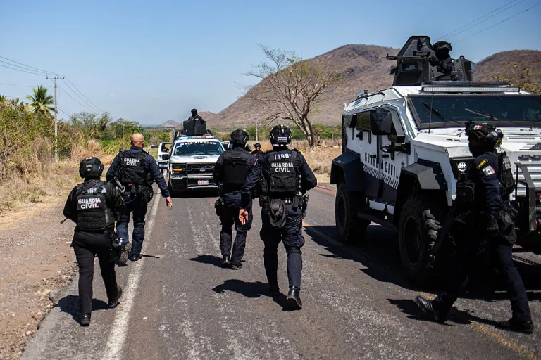 Members of the Civil Guard of Michoacan patrol a highway supported by armored vehicles after a wave of violence in the town of Aguililla, the birthplace of drug kingpin Nemesio Oseguera, leader of the Jalisco New Generation Cartel (CJNG) in Tierra Caliente, Mexico, on February 24, 2026. Mexican President Claudia Sheinbaum on February 24 dismissed risks to fans visiting Guadalajara, one of the venues for the 2026 World Cup, after a drug cartel riot caused fear in the city and much of the country on February 22. (Photo by Enrique Castro / AFP via Getty Images)