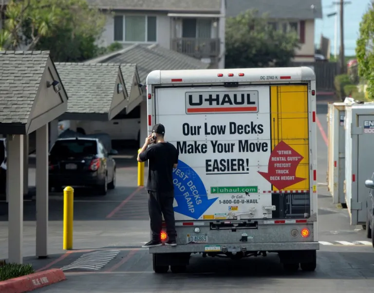 A man talks on his cell phone while riding on the back of a moving truck as residents evacuate apartments atop an eroding cliff in Pacifica, California on January 26, 2016. - Storms and powerful waves caused by El Nino have been intensifying erosion along nearby coastal bluffs and beaches in the area. (Photo by JOSH EDELSON / AFP) (Photo by JOSH EDELSON/AFP via Getty Images)