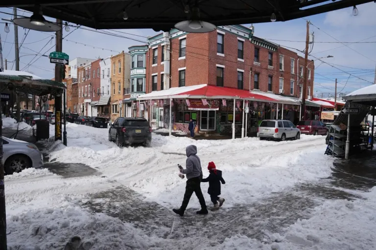 People cross a snow covered street in the aftermath of a winter storm in Philadelphia, Monday, Jan. 26, 2026. (AP Photo/Matt Rourke)