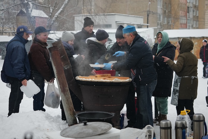 Volunteer Marat Darmenov, center right, serves free hot food to Kyiv residents during a blackout caused by Russia's regular air attacks on the country's energy system in Kyiv, Ukraine, Saturday, Feb. 7, 2026. (AP Photo/Sergei Grits)