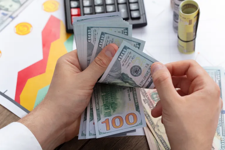 A person holds a stack of $100 bills.
