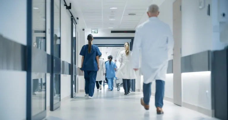 Hospital Hallway with Doctors, Nurses and Specialists in Hospital. Female and Male Physicians, Surgeons, Healthcare Officials Walk Together in Corridor with Their Back to Camera health healthcare