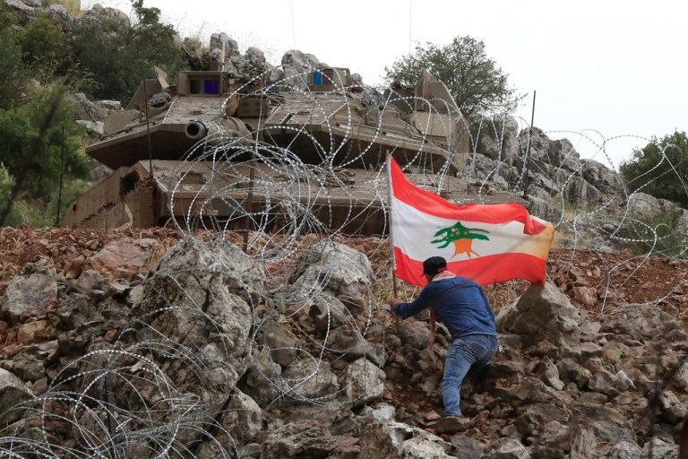 A Lebanese protester sets a Lebanese flag under a Israeli Merkava tank