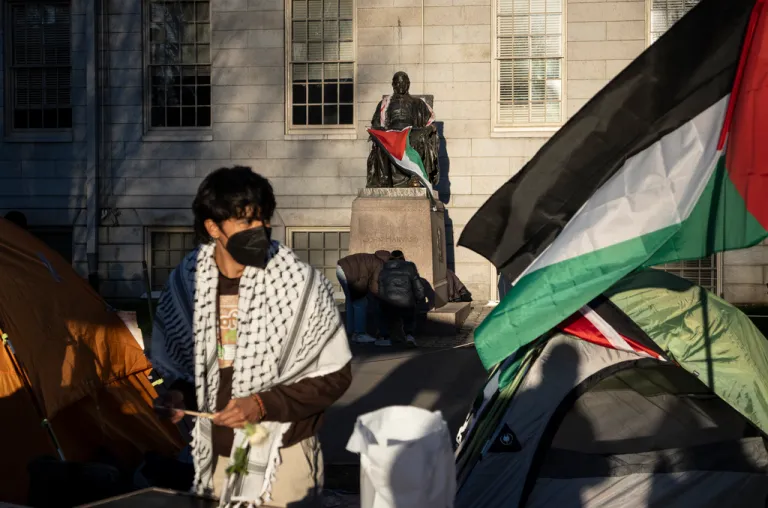 A student protester stands in front of the statue of John Harvard.