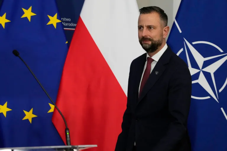 Wladyslaw Kosiniak-Kamysz stands in front of a Polish flag, a NATO flag, and a European Union flag