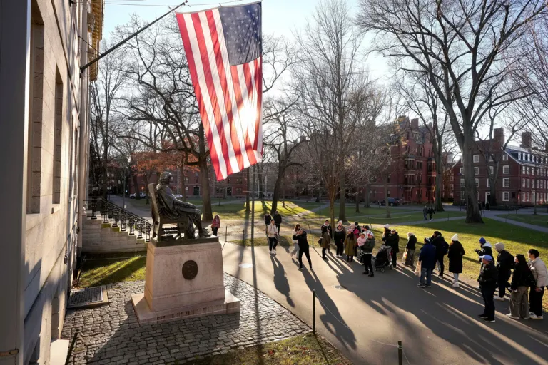 People take photos near a John Harvard statue on the Harvard University campus.