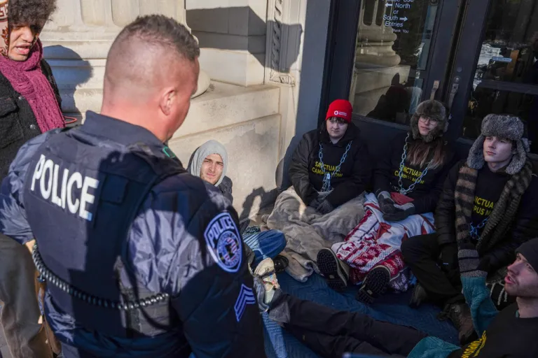 A University of Minnesota Police officer threatens student protesters with arrest for chaining themselves to a door on campus during an anti-ICE protest, on Friday, Feb. 6, 2026, in Minneapolis. (AP Photo/Ryan Murphy)