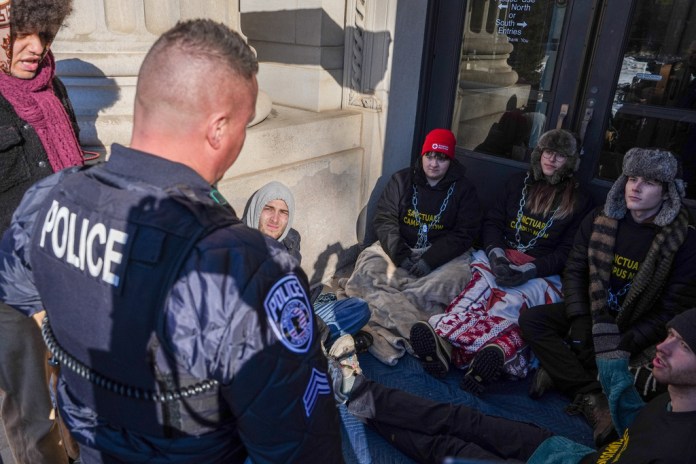 A University of Minnesota Police officer threatens student protesters with arrest for chaining themselves to a door on campus during an anti-ICE protest, on Friday, Feb. 6, 2026, in Minneapolis. (AP Photo/Ryan Murphy)