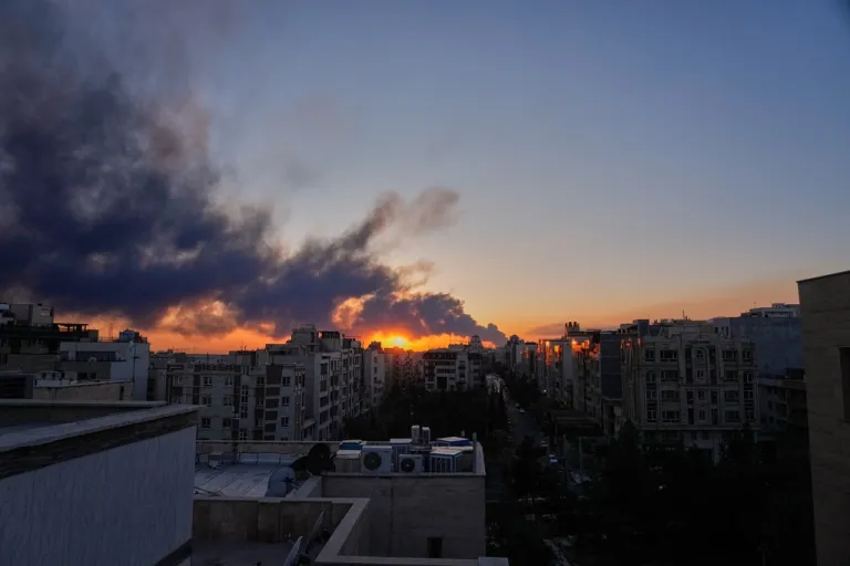 The sun sets behind a plume of smoke rising after a U.S.-Israeli military strike in Tehran.
