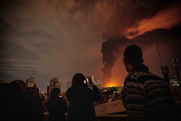 Residents watch and take pictures as flames and smoke rise from an oil storage facility struck as attacks hit the city during the U.S.–Israeli military campaign in Tehran