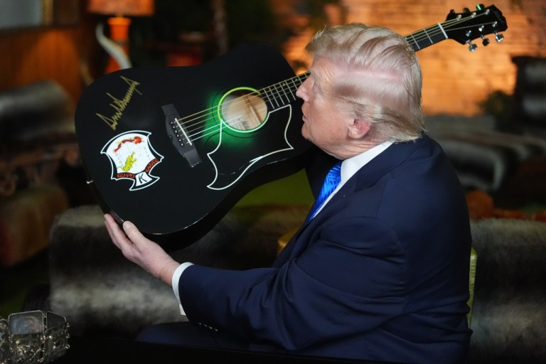 President Donald Trump holds up replica of a Elvis Presley guitar he had just signed, in the Jungle Room at Graceland.