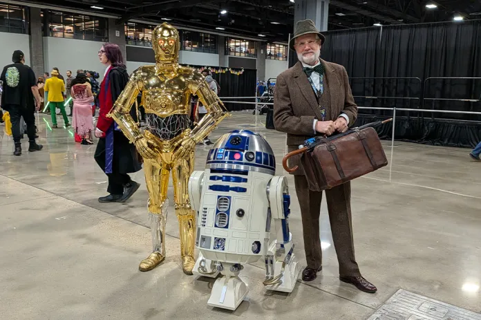 C-3PO, R2-D2, and a person posing for a picture.