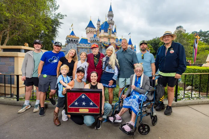 Anaheim, Calif. (March 31, 2026) - 100-year-old World War II veteran Charles Cram, alongside his family, in front of Sleeping Beauty Castle in Disneyland Park at Disneyland Resort. Cram served as a U.S. Navy Pharmacist’s Mate Second Class with the 5th Marine Division during the Battle of Iwo Jima. He was honored at the theme park’s daily Flag Retreat Ceremony for his service to country. (Photo credit: Disney)