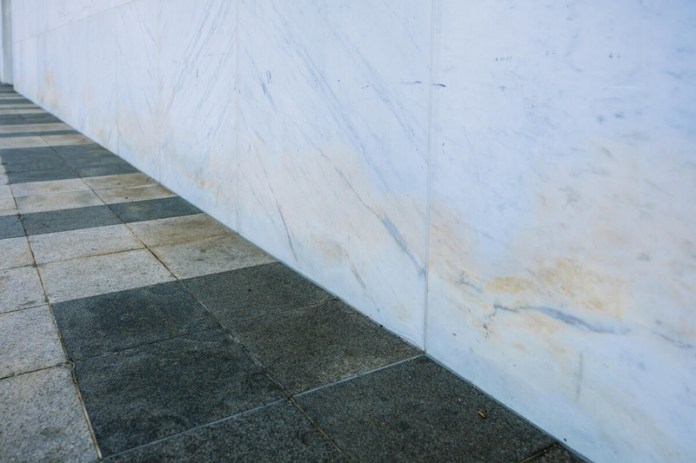 Improper installation traps moisture behind stone panels, causing staining and internal corrosion. Panels and granite paving slabs will be replaced with corrected drainage systems.