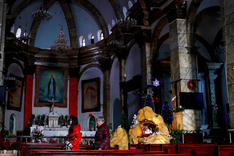 Chinese women walk past a decoration displaying a Baby Jesus doll part of a Nativity scene.