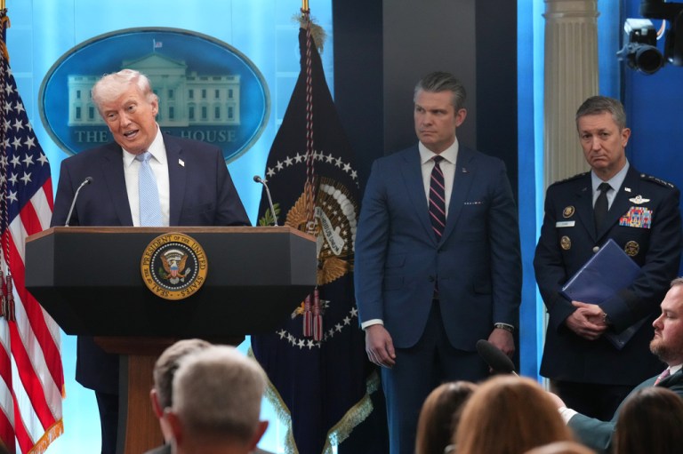 President Donald Trump, War Secretary Pete Hegseth, and Gen. Dan Caine stand onstage in the White House briefing room.