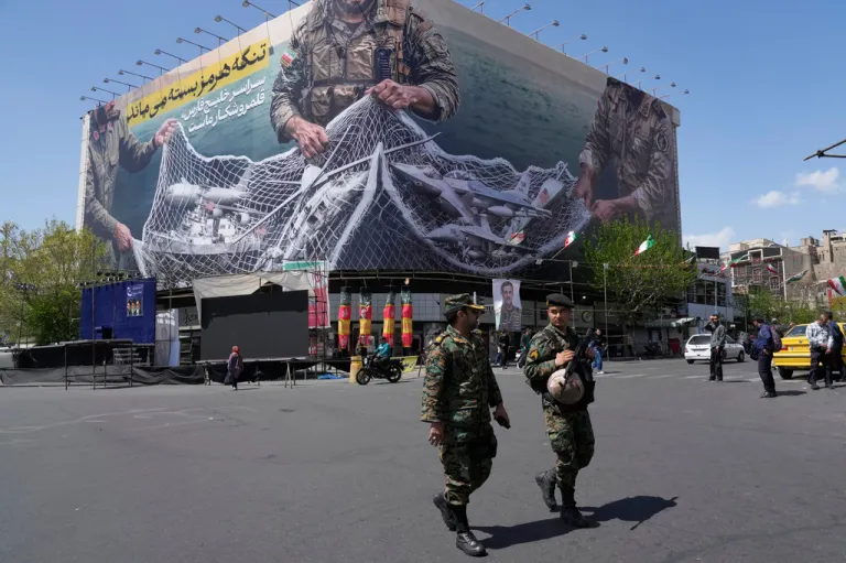 Two police officers walk in front of an anti-U.S. billboard depicting American aircraft being caught by Iranian armed forces in a fishing net beneath the words in Farsi, 