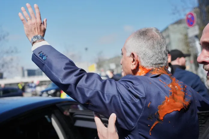 Reza Pahlavi waves to supporters with the red liquid on his back
