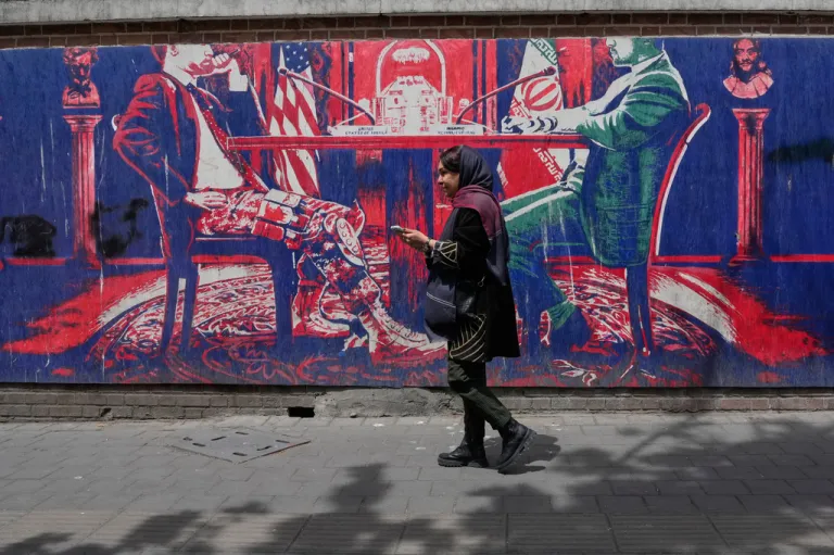 A woman walks past an anti-U.S. mural painted on the wall of the former U.S. embassy mocking Iran and United States talks, in Tehran, Iran, Saturday, April 25, 2026.