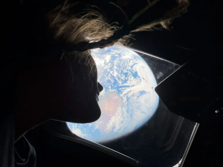 NASA astronaut and Artemis II mission specialist Christina Koch peers out of one of the Orion spacecraft's main cabin windows, looking back at Earth.