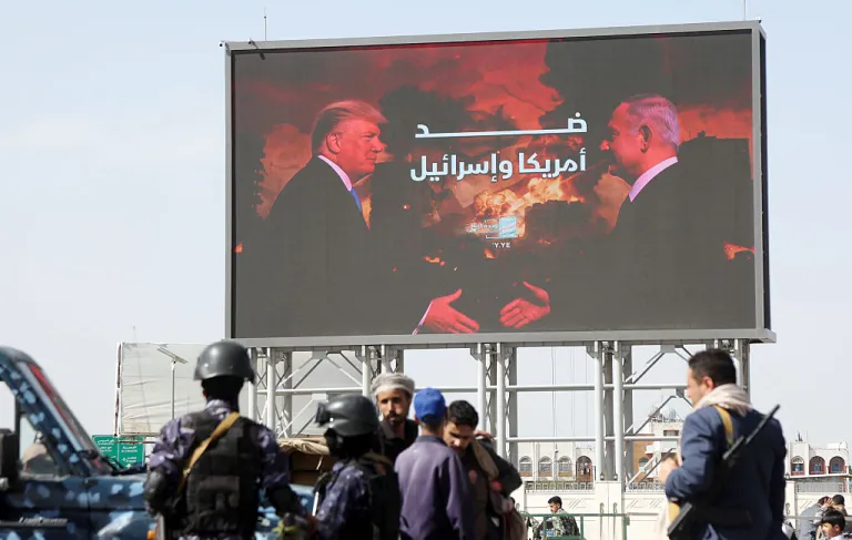 Yemen's Houthi security soldiers stand next to a billboard depicting the Israeli Prime Minister Benjamin Netanyahu and U.S. President Donald Trump, during a demonstration staged to show solidarity with Iran on April 3, 2026 in Sana'a, Yemen. Yemen's Iran-backed armed Houthi group has warned they will move to shutter the Bab Al-Mandeb Strait through missile-drone attacks if Gulf nations join the US-Israel war on Iran. (Photo by Mohammed Hamoud/Getty Images)