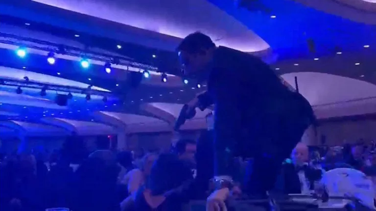 A screen grab taken from a video filmed by an AFP reporter shows an armed agent climbing over chairs as they move to the stage after loud bangs were heard during the White House Correspondents' dinner at the Washington Hilton in Washington, DC, on April 25, 2026. Shots were fired as US President Donald Trump attended a press dinner in Washington on Saturday night, witnesses and AFP reporters confirmed. Loud bangs were heard and guests at the black-tie White House Correspondents' Dinner scrambled to hide under tables. (Photo by Danny KEMP and AFPTV teams / AFP via Getty Images)