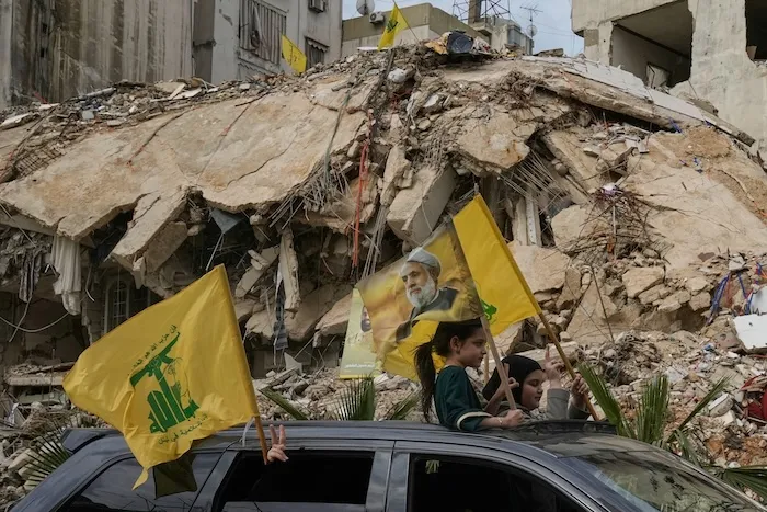 Displaced residents wave Hezbollah flags, including one bearing a picture of its leader, Naim Qassem.