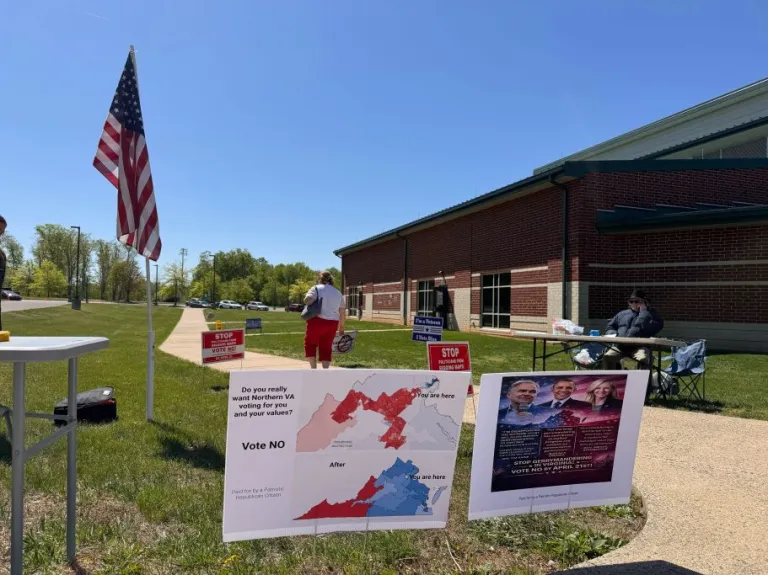 Virginia redistricting vote signs next to two people on a sidewalk and American flag outside of a high school building