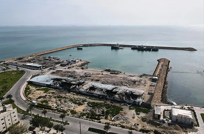 Backdropped by ships in the Strait of Hormuz, damage caused by airstrikes is seen on a fishing pier in the port of Qeshm island, Iran on April 13. (Asghar Besharati/AP)