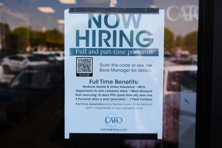 A now hiring sign sits on the window of a retail clothing store in Garland, Texas on March 23, 2026.