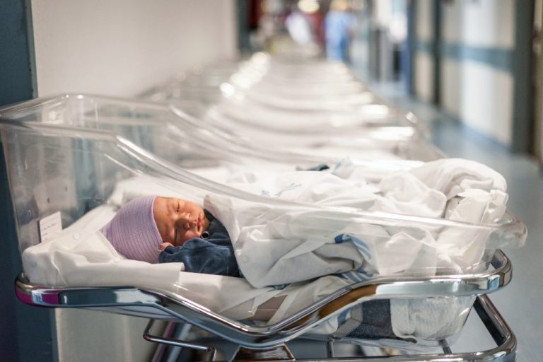 Newborn baby boy in his small transparent portable hospital bed.