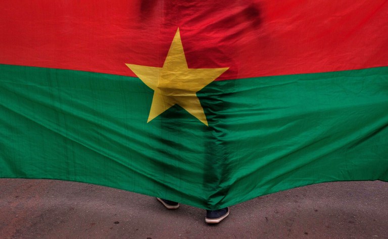 The Burkina Faso national flag with a man standing directly behind it is seen during a memorial ceremony in Ouagadougou, Burkina Faso, Jan. 23, 2016. (AP Photo/Theo Renaut)