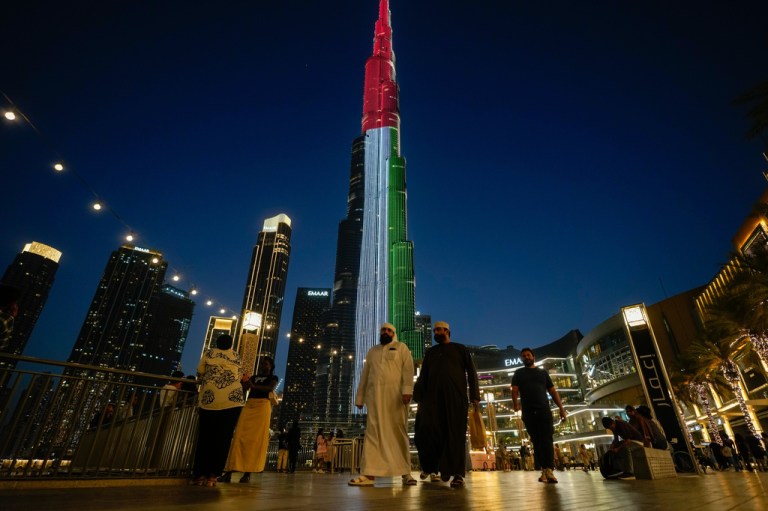 People walk as Burj Khalifa, the world's tallest building, is illuminated with the UAE national flag colors in Dubai, UAE.