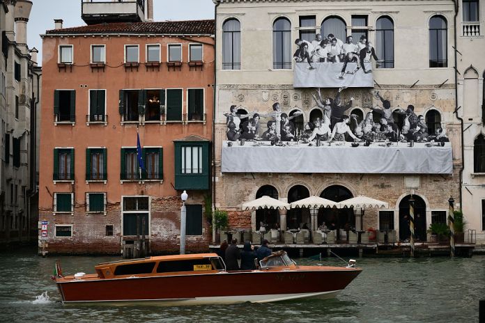 A picture shows "Il Gesto" by French artist JR, on the facade of Ca' del Mosto, near Rialto bridge during the 61st Venice Art Biennale in Venice on May 5, 2026. The palazzo's facade becomes the surface for a large-scale temporary artistic installation inspired by Paolo Veronese "The Wedding at Cana" from the collection of the Musee du Louvre, originally created for the monastery of San Giorgio Maggiore in Venice. (Photo by MARCO BERTORELLO / AFP via Getty Images) / RESTRICTED TO EDITORIAL USE - MANDATORY MENTION OF THE ARTIST UPON PUBLICATION - TO ILLUSTRATE THE EVENT AS SPECIFIED IN THE CAPTION