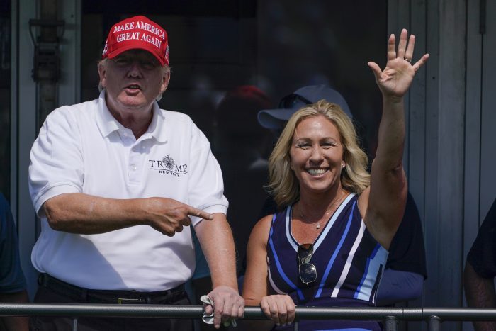 Rep. Marjorie Taylor Greene (R-GA) waves while former President Donald Trump points to her.
