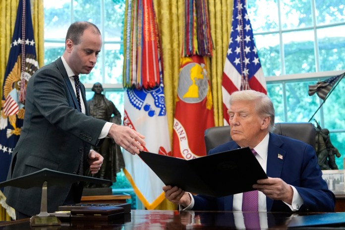 White House staff secretary Will Scharf hands President Donald Trump an executive order to sign