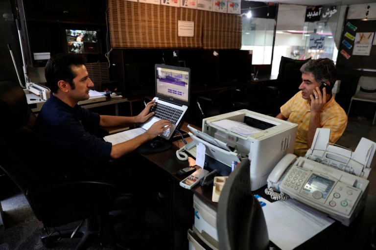 An internet cafe manager works on his computer as a man talks on his cell phone in Tehran.